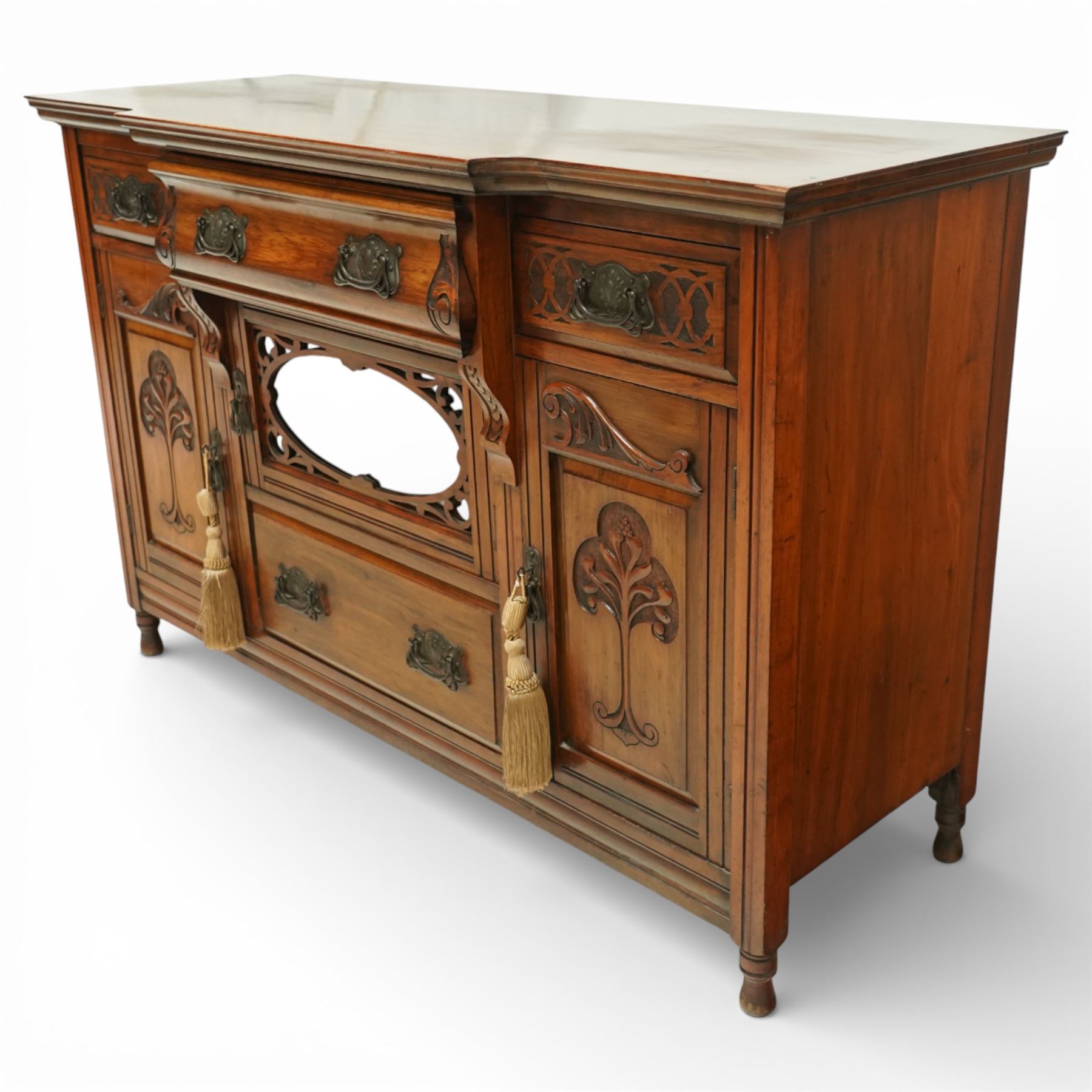 Late 20th century Art Nouveau walnut sideboard, the moulded rectangular top above a run of three drawers, the outer drawers with blind fretwork decoration and applied metal handles, the centre drawer with scroll carved terminals, below a central mirrored cupboard door with oval panel and pierced surround, flanked by carved panel doors with sinuous foliate motifs, on turned supports