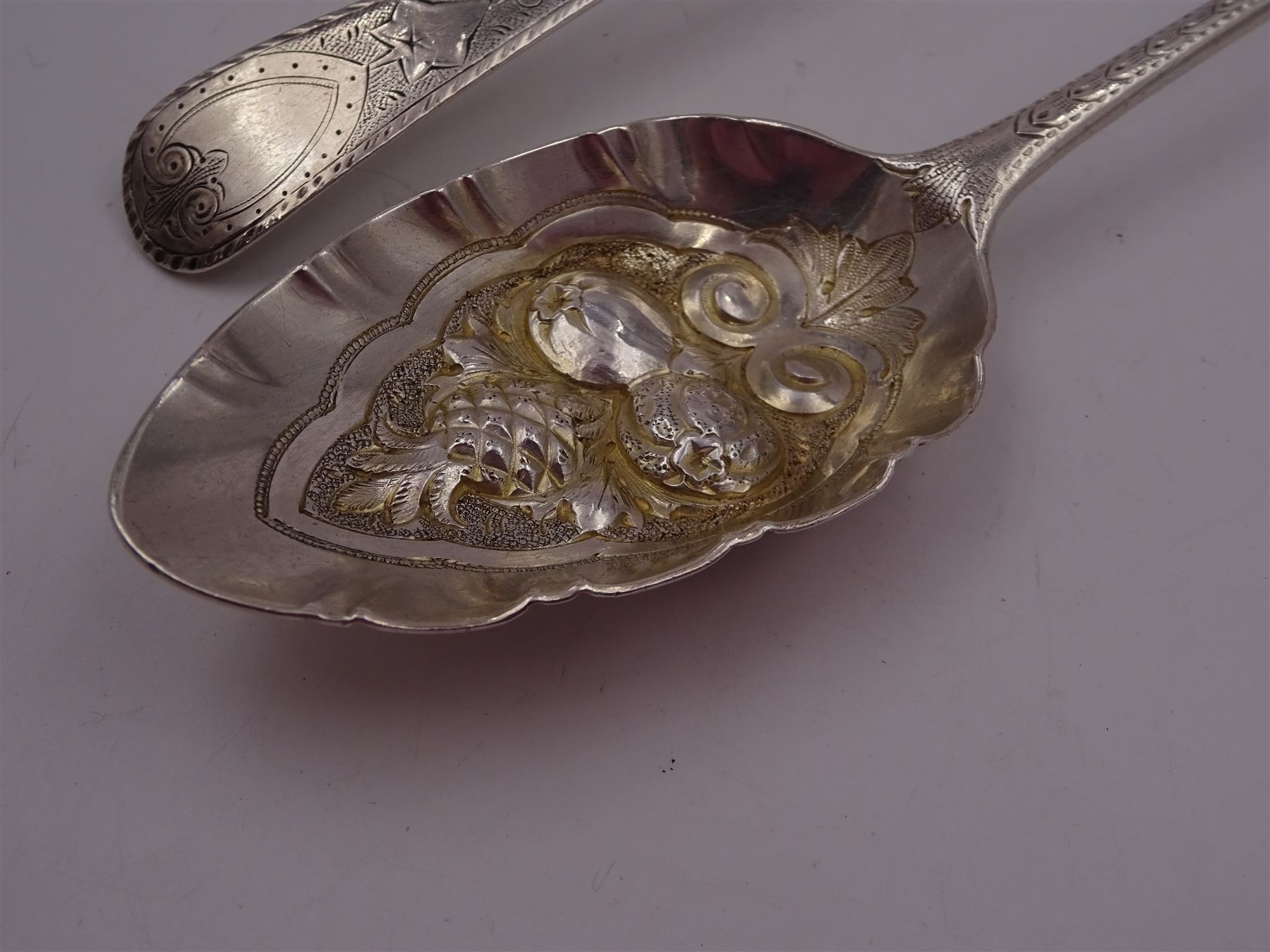 George IV silver fruit serving spoon, the bowl embossed with fruits, with engraved vine leaf decoration to handle, hallmarked London 1789, together with a very similar earlier example, hallmarks worn and indistinct