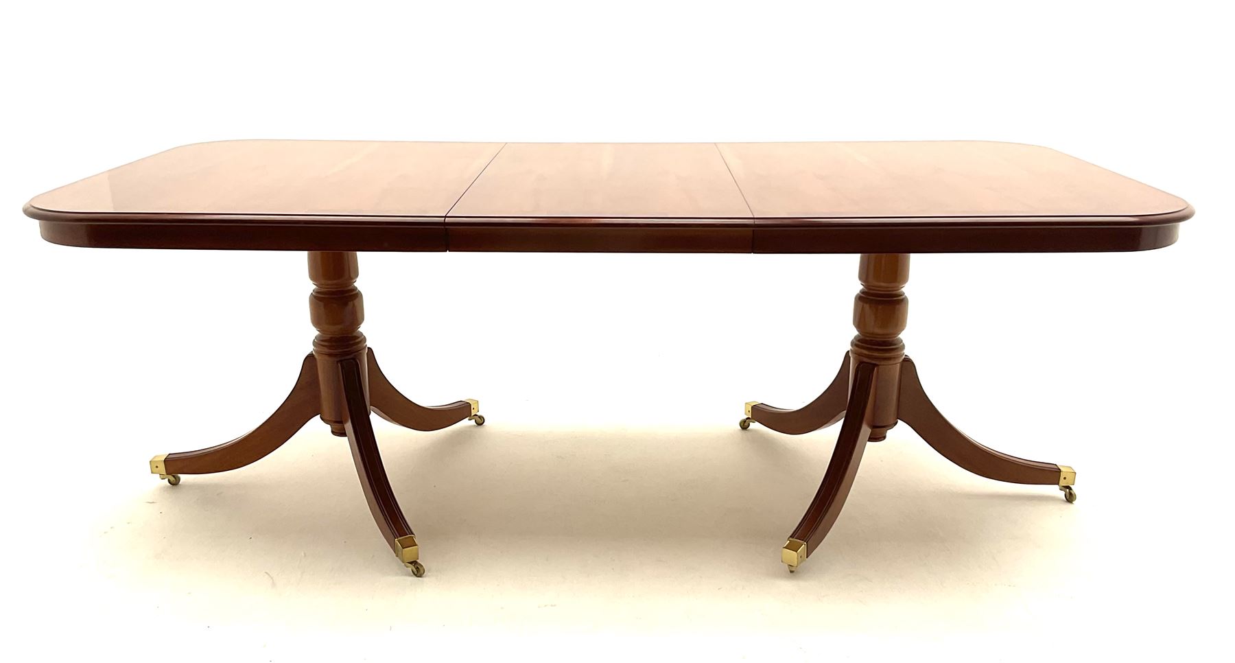 Yew wood twin pedestal extending dining table, shaped supports and brass castors (W216cm, D100cm, H77cm) and six (4+2) chairs, shaped back and upholstered in patterned fabric raised on fluted supports (W52cm)