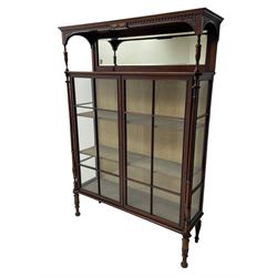 Late 19th century mahogany bookcase, the canopy top with moulded dentil cornice and fan carved spandrels on turned and reeded supports, rectangular bevelled mirror back, two astragal glazed doors with reed moulded slips enclosing fabric lined interior with two shelves, flanked by turned and reed carved columns with acanthus leaf capitals, on turned and carved feet