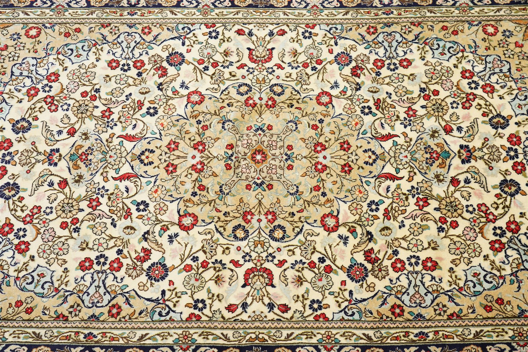 Central Persian Kashan hand-knotted carpet, ivory ground with a central floral medallion with an all-over design of scrolling vinery, palmettes, and flowering sprays i tones of madder red, cobalt, navy blue and sage green, with conforming spandrels, main border of deep indigo ground with repeating palmettes and stylized floral heads, flanked by narrow guard stripes, with cotton fringe ends, with cotton fringe ends 