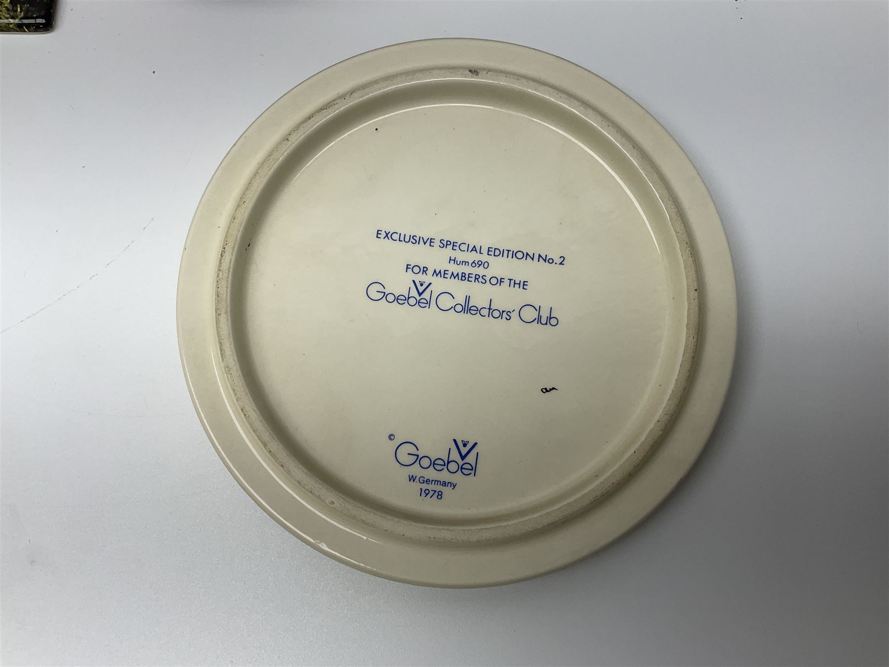 Two ceramic Hummel postcards by Goebel, both displayed on wooden easels, together nine Hummel eggs, set of four Hummel School Days plates, on wooden hanging rack, Goebel Collectors Club Member plaque etc