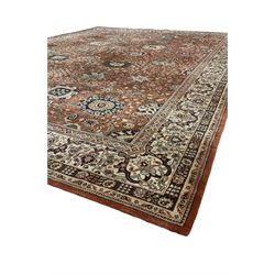 Persian design carpet, rust ground field decorated with large stylised plant motifs surrounded by smaller floral motifs, repeating trailing border