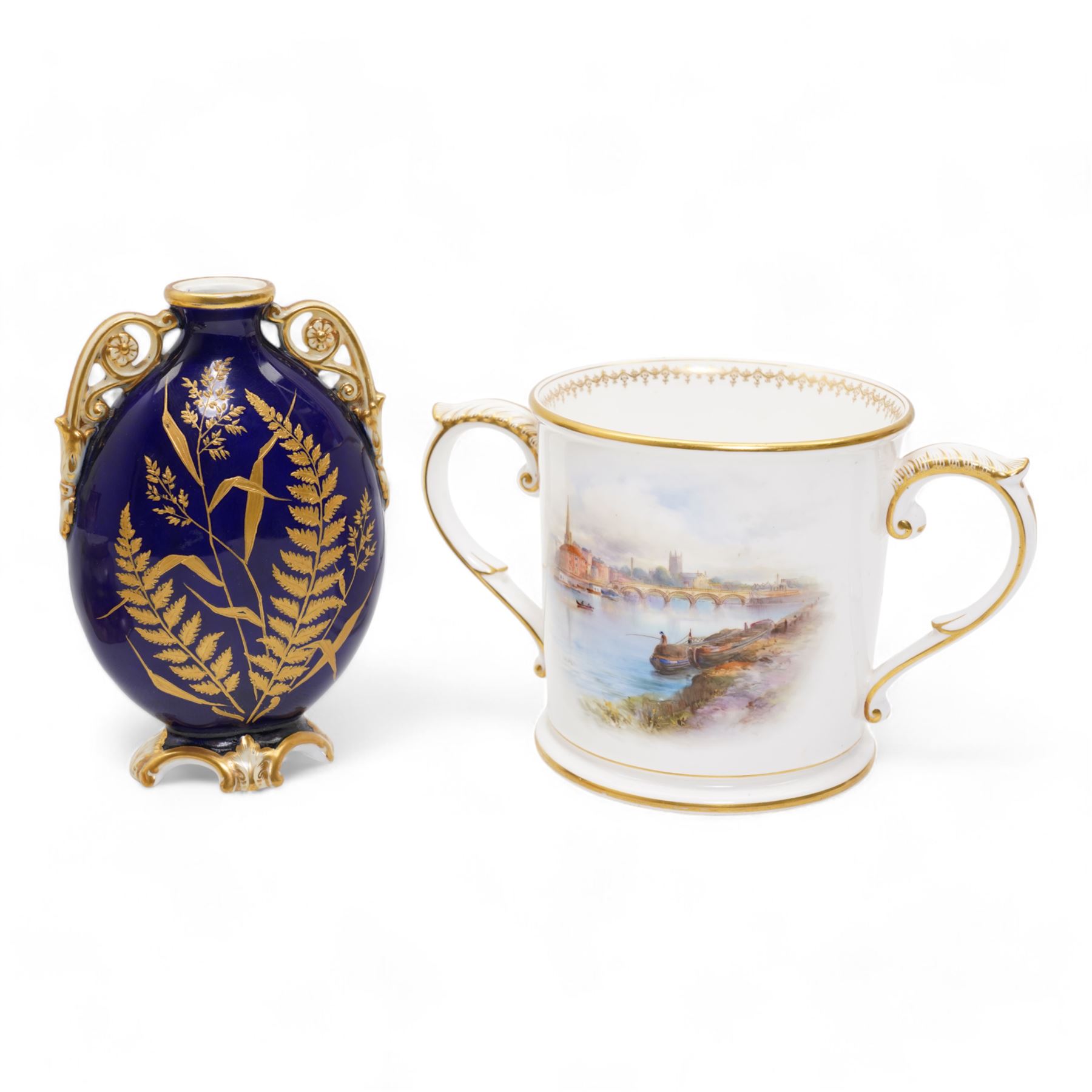 Early 20th century Royal Worcester loving cup, circa 1906, painted with a view of the River Severn and flowers to the reverse, H13cm, Grainger & Co. Worcester twin handled vase, the oval body painted in the Aesthetic style with ferns and grasses in gilt, against a cobalt blue ground, with scrolled handles and quatrefoil foot, H17cm (2)