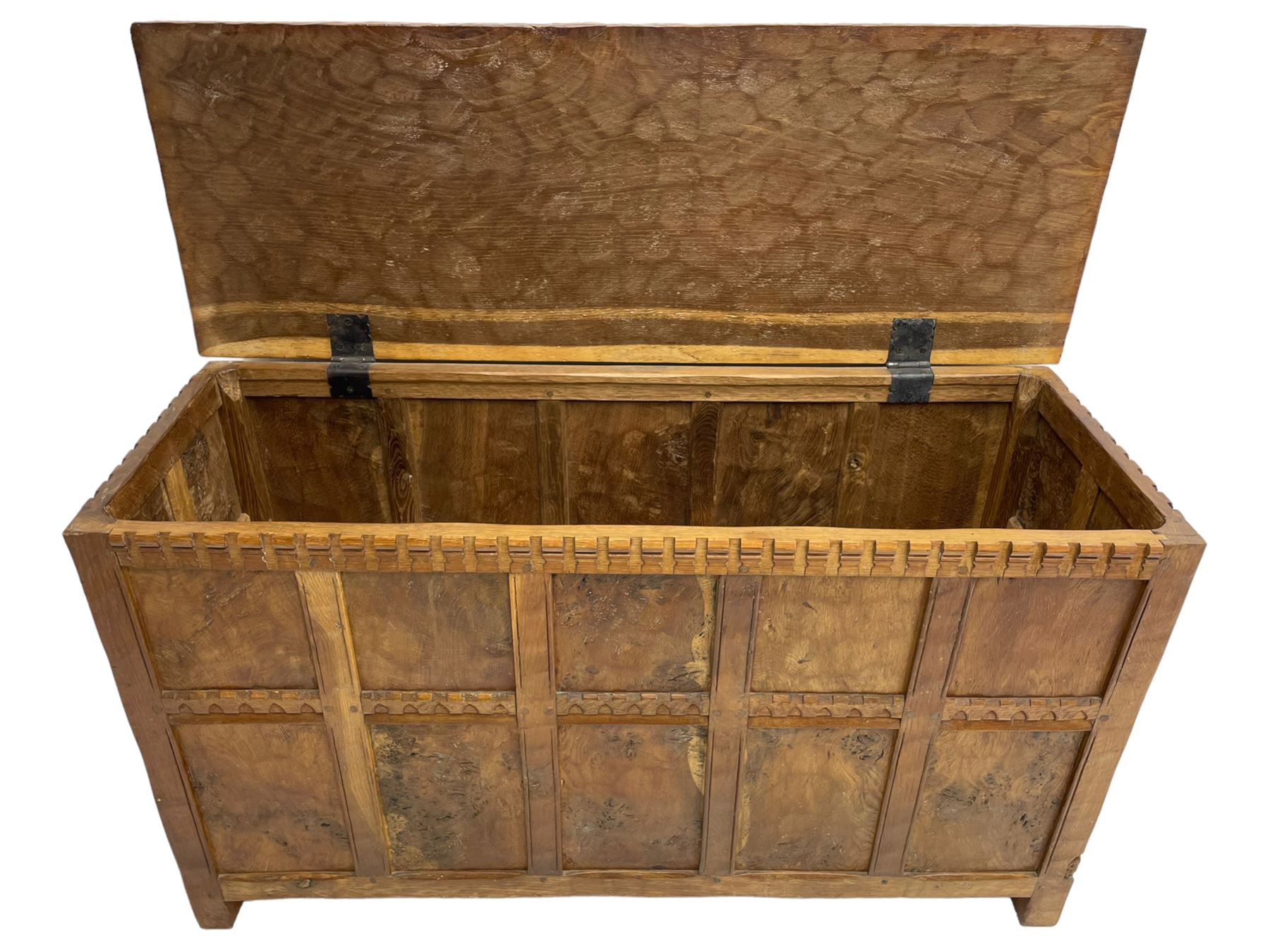 Gnomeman - oak blanket box, all-over adzing, the hinged top over figured and burr panelled front, decorated with carved crenellations and arcade, carved with gnome signature, pierced handles to each end forming the central rail, wrought metal hinges, on stile supports, by Tom Whittaker, Littlebeck, Whitby