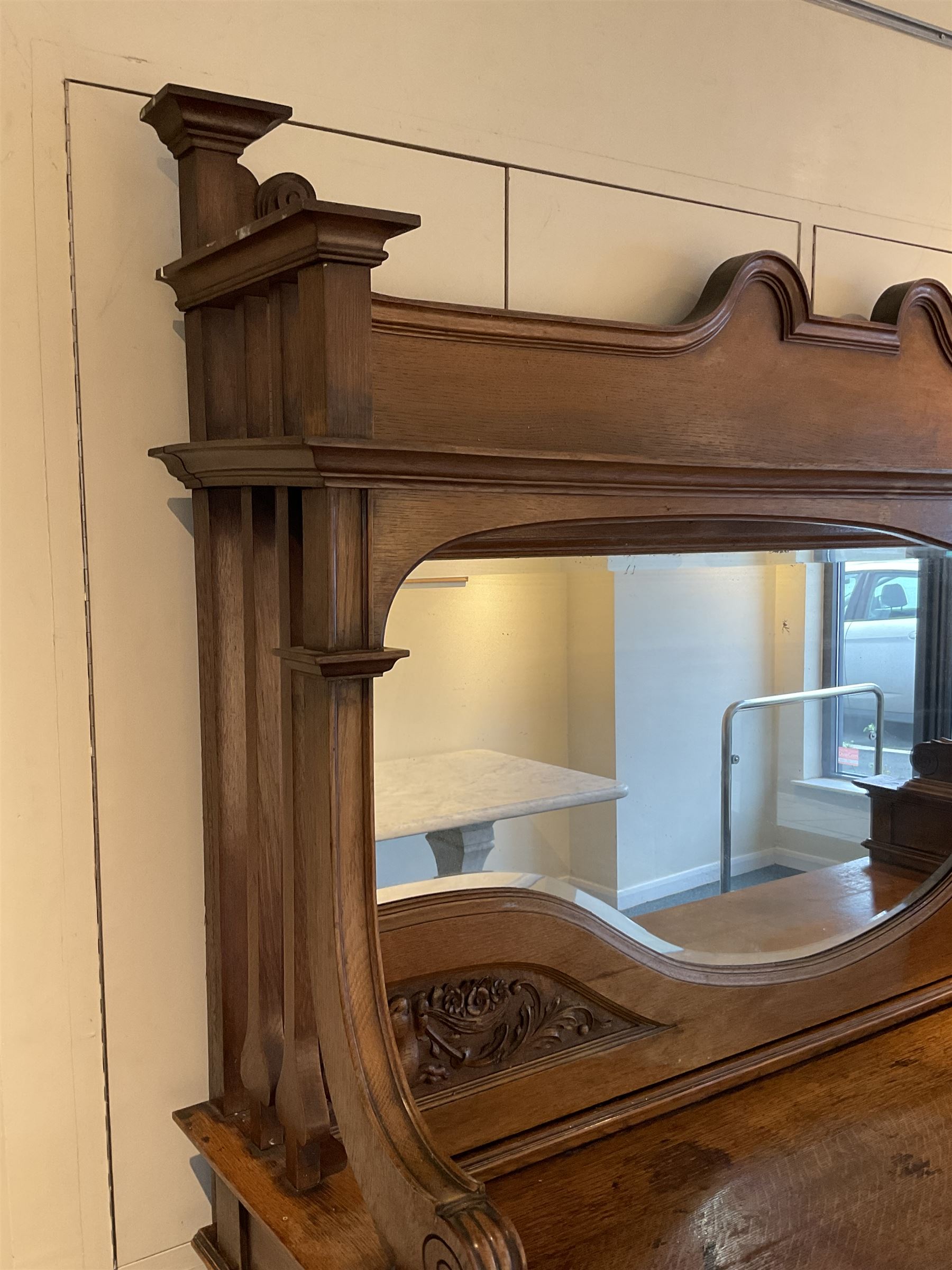 Late 19th century Arts & Crafts period oak mirror back sideboard, shaped bevelled mirror back carved with foliate scrolls and flower heads, down swept supports with elongated club-shaped uprights, moulded rectangular top over two drawers and three cupboards, the drawer fronts with copper handles decorated with sailing ships, panelled doors carved with mythical beasts, flowerheads and foliage, on moulded block feet
