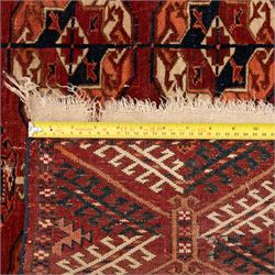 Persian Bokhara crimson ground rug, the field decorated with five rows of repeating Gul motifs with interspersed geometric design, enclosed by a guard band of further geometric-style Gul designs comprised of hook motifs