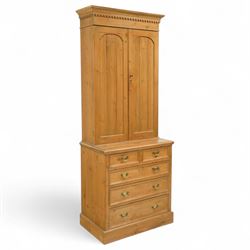 Early 20th-century pine gun cabinet with later fitted shelves, of two-part construction, upper cupboard moulded and dentil cornice above two panelled doors revealing three removable shelves and circular recesses for gun barrels at the top, lower section with two short and three long graduated drawers with brass swan neck handles on plinth base 