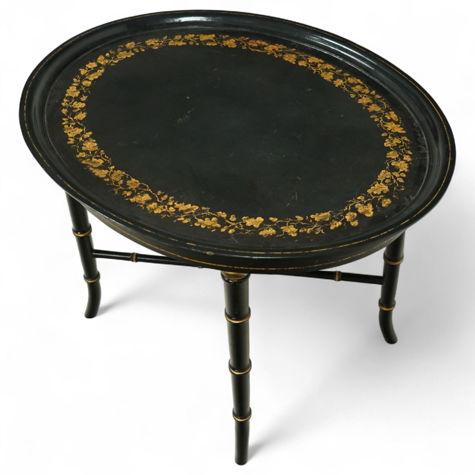Regency style oval toleware tray table, the black lacquered top with gilt floral decoration, on ebonised faux bamboo frame with stretcher supports