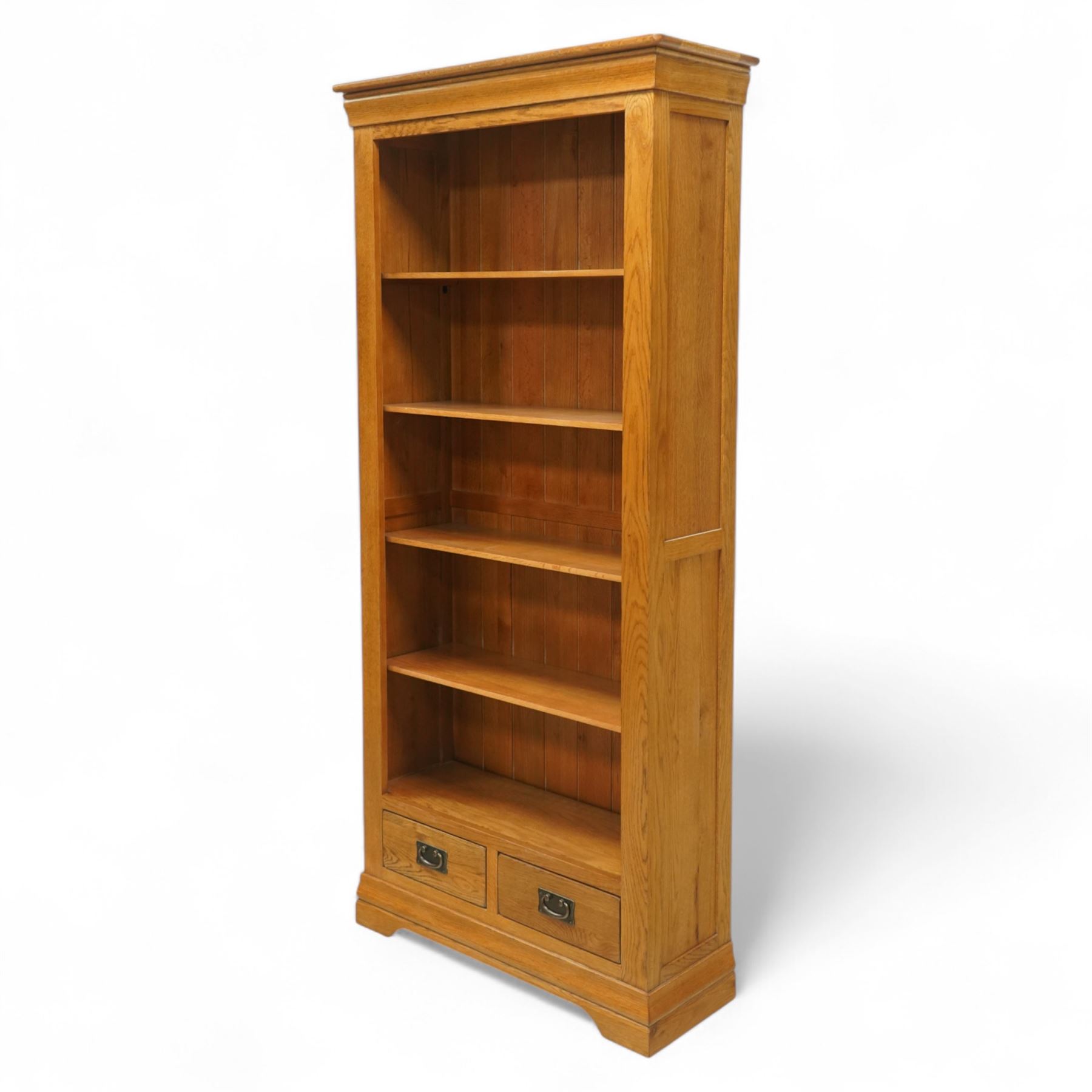 Contemporary oak bookcase, with moulded cornice above open shelved interior, fitted with four adjustable shelves and two short drawers with inset brass handles, panelled sides, plinth base