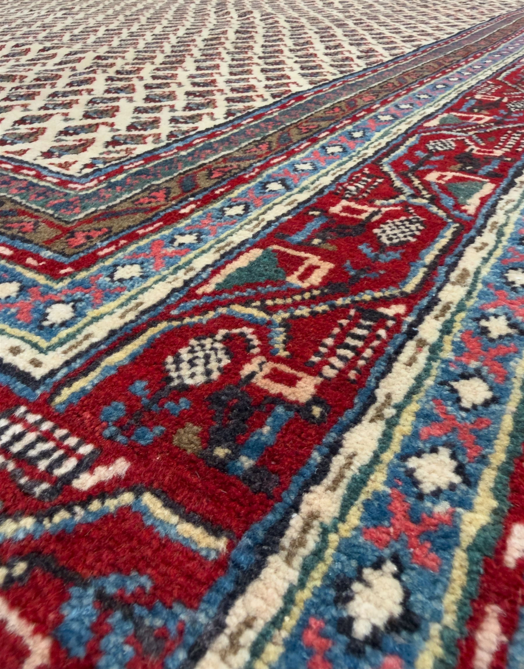 Northwestern Persian Bottehmir hand-knotted rug, ivory field with an all-over design of boteh motifs arranged in diagonal rows within multiple borders and a primary madder red field with stylized vine and flowerhead motifs, 320cm x 214cm 