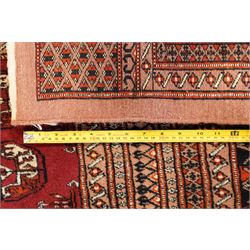 Large Afghan Bokhara crimson ground carpet, the field with rows of repeating Gul motifs and geometric design, enclosed by multiple repeating geometric guard bands