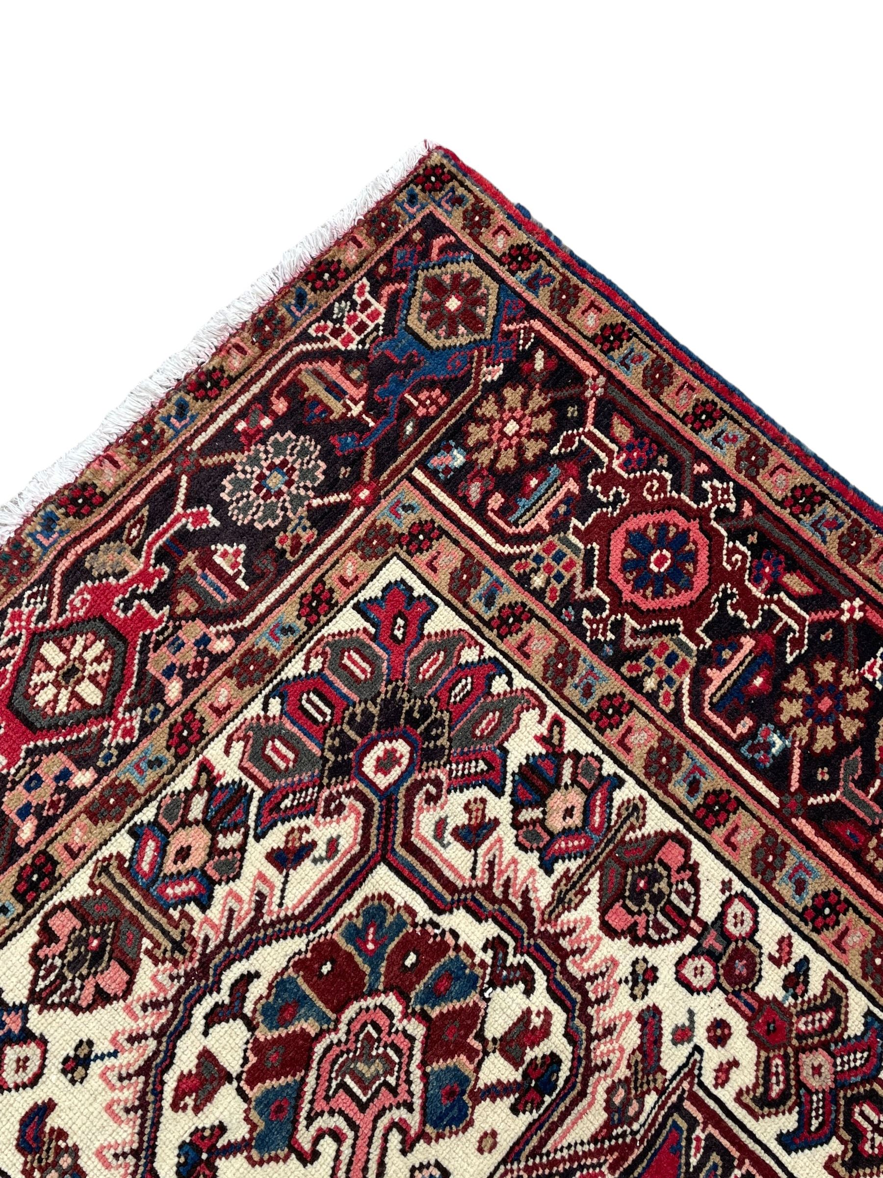 Persian Heriz red ground rug, central scrolled medallion on dark ground decorated with floral motifs, the surrounding field decorated with stylised plant motifs and smaller geometric symbols, guarded border with repeating pattern punctuated with rosettes and flower heads 