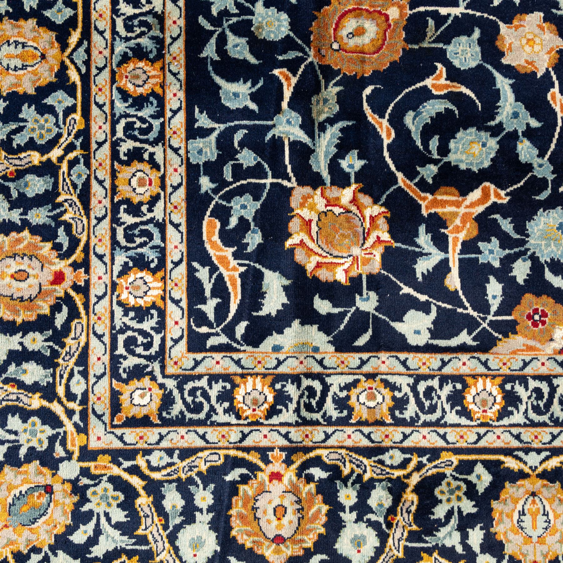 Persian Kashan carpet, navy field with an all-over design of scrolling vines, palmettes and rosettes in gold and pale blue, enclosed by multiple floral borders with stylised palmette motifs, originating from Central Iran