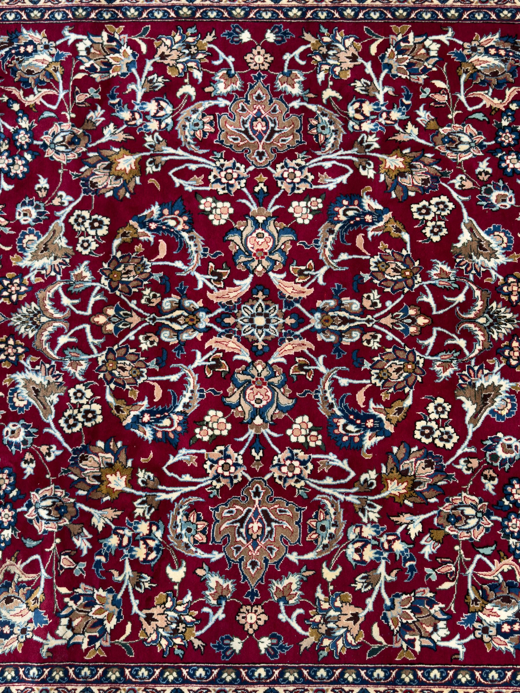 Central Persian Yazd hand-knotted rug, madder red field with scrolling vines, palmettes, and rosettes around a cusped lozenge medallion within a blue ground border of palmettes and flowerheads, 366cm x 250cm