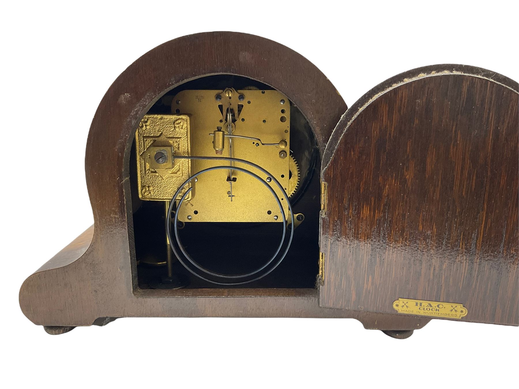 An oak cased 1930’s eight-day German mantle clock manufactured by HAC (Hamburg Amerikanische Uhrenfabrik), spring driven movement with a recoil anchor escapement striking the hours and half hours on a coiled gong, in round case with silvered chapter ring with Arabic numerals and minute markers, steel spade hands within a brass bezel and convex glass. With a presentation plaque to the front of the case. With pendulum.


