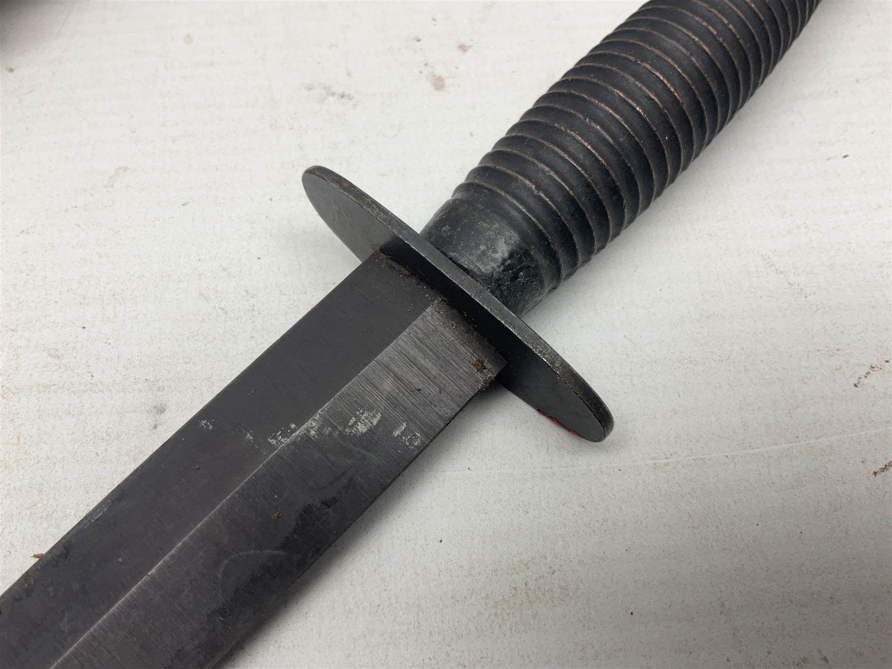 Third Pattern Commando Knife or Dagger with 17.5cm flattened diamond section blade and regulation black painted ribbed copper hilt with brass pommel nut; stamped William Rodgers Sheffield England to the cross-piece; in black painted brass mounted leather scabbard L34.5cm overall