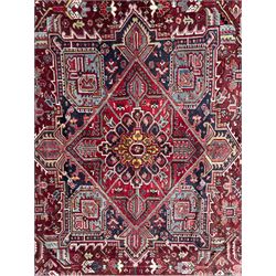 Northwestern Persian Heriz carpet, the madder red field centred by a large octofoil medallion with serrated edge, flanked by ivory stepped spandrels and geometric floral motifs in indigo, ochre and sky blue, enclosed by a navy border of rosettes and angular vines, from the region of Heriz