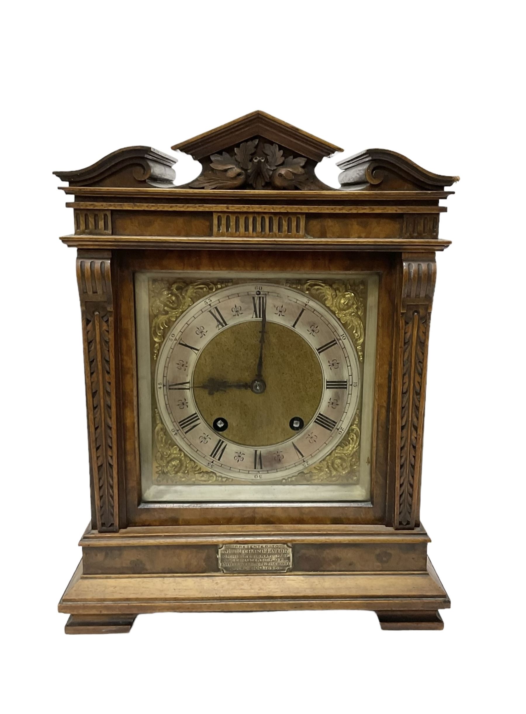 Lenzkirch - Late 19th century 8-day German mantle clock in a walnut veneered case with an architectural pediment, square brass dial, cast spandrels, matted dial centre, silvered chapter ring and fleur-di-Lis hands, with a twin train movement chiming the quarters on two coiled gongs and striking the hours on one. With Key and pendulum. Silver presentation plaque dated 1896.