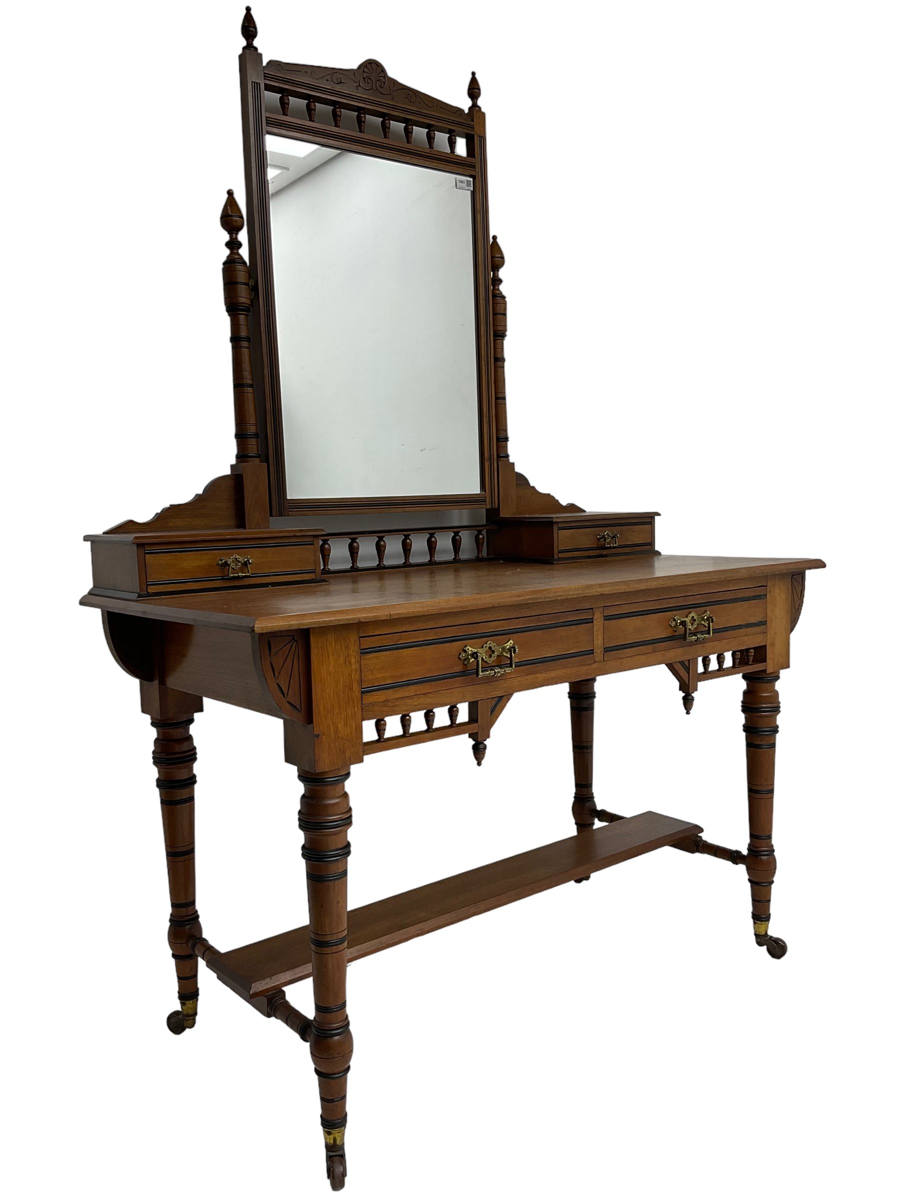 Late Victorian Aesthetic Movement walnut and inlaid ebony dressing table, swing mirror back with shell carving and spindle support rail, fitted with two trinket drawers and single frieze drawer, raised on ring turned supports with castors