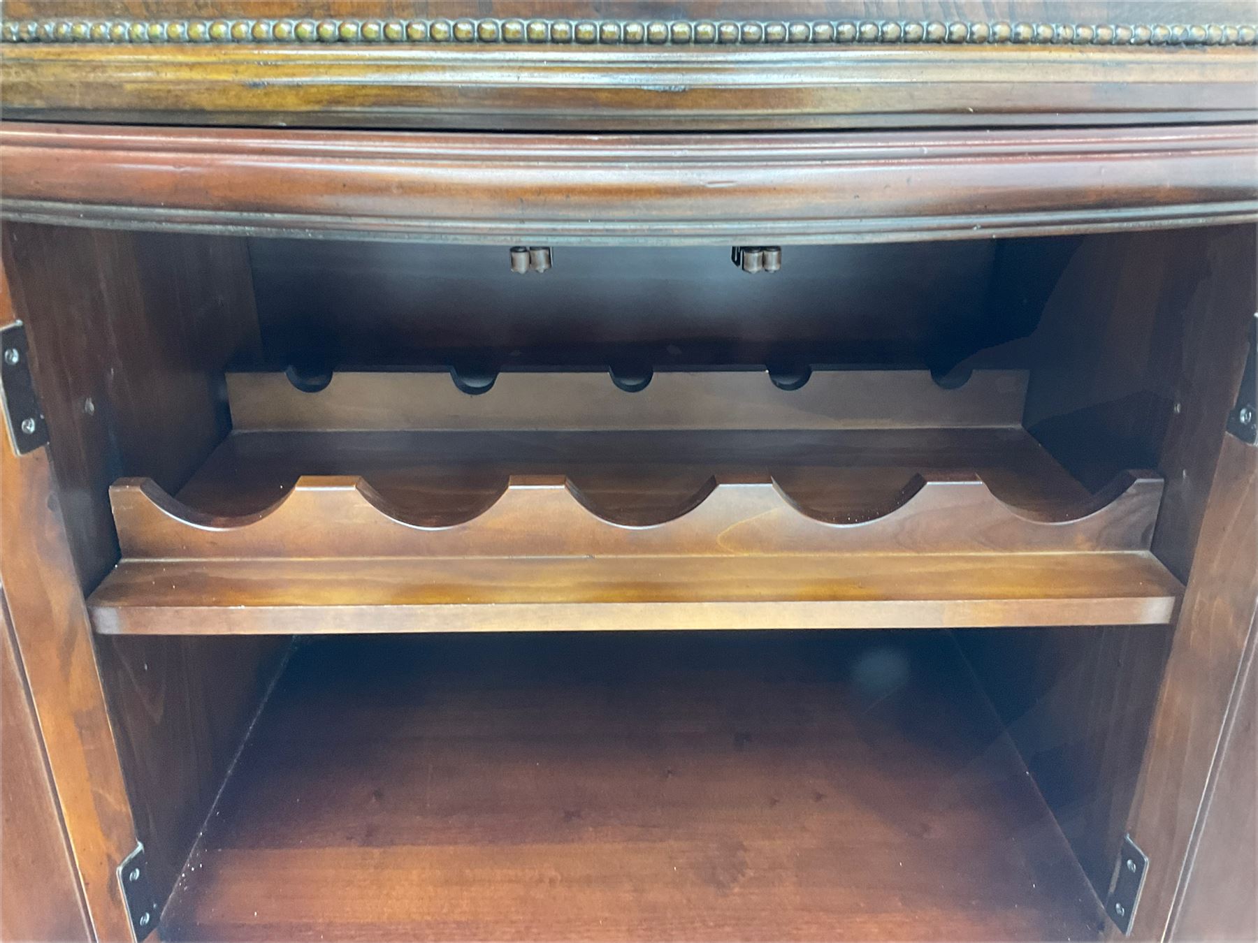  Kevin Charles American walnut demi lune display cabinet with illuminated interior, projecting cornice, two bevel edge glazed doors enclosing two adjustable shelves above single drawer and four cupboard doors with wine rack, carved scrolling supports