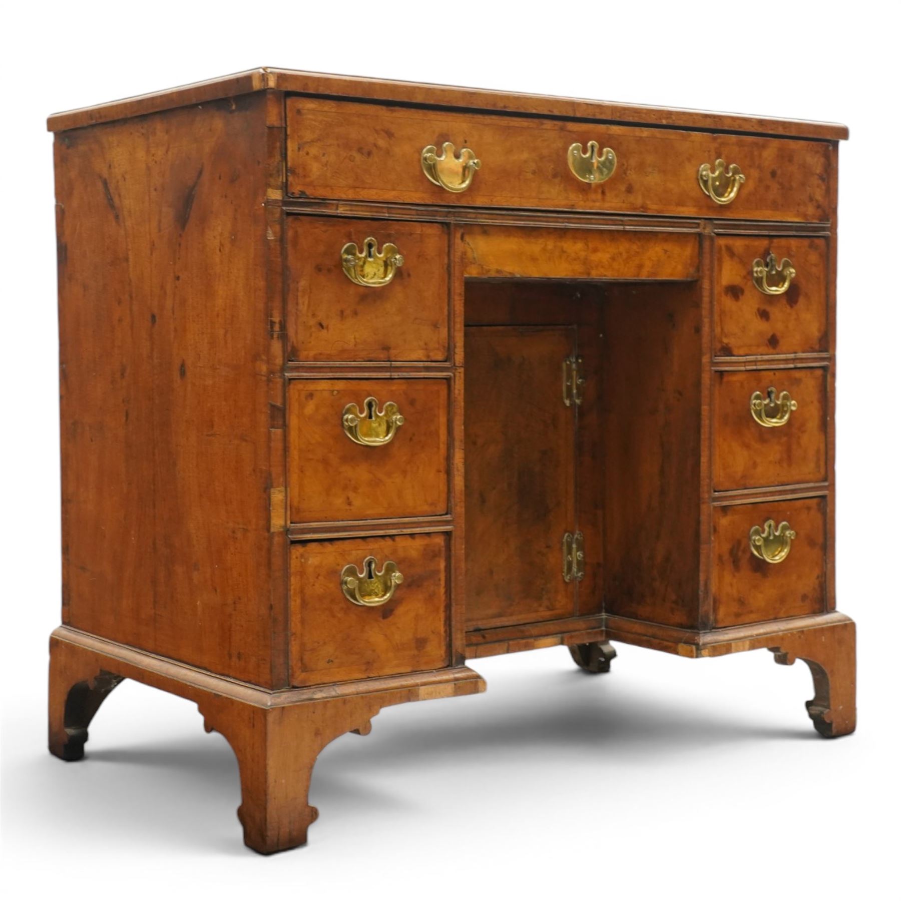 George II figured walnut kneehole desk, the rectangular book-matched veneer top with feather and cross-banding, fitted with single frieze drawer over a short drawer and central recessed cupboard, flanked by three drawers to each side, lower moulded edge on bracket feet