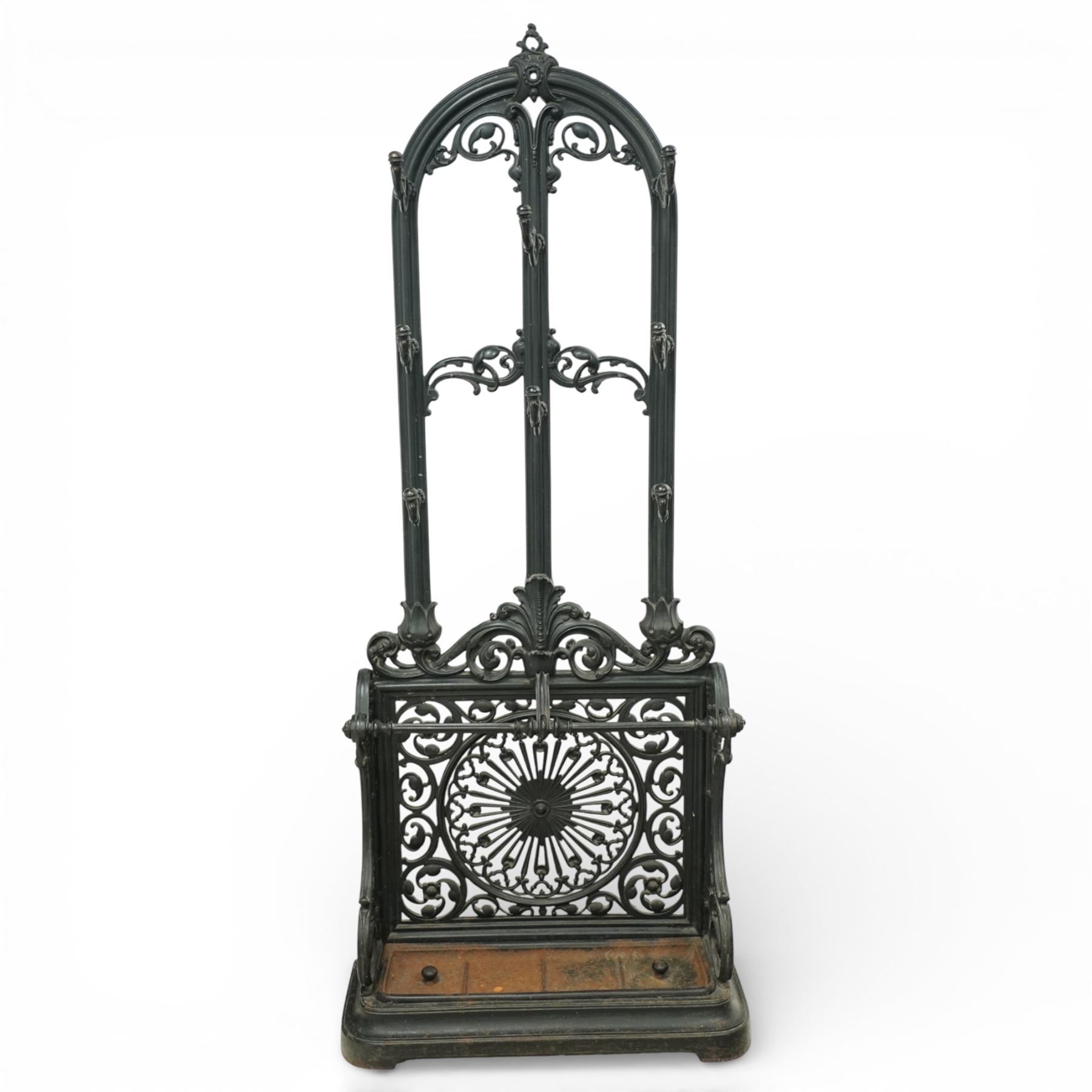 Late 19th century cast iron stick stand, the arched back with scrolling foliate decoration, fitted with multiple hooks, the lower section with pierced panels centred by a radiating sunburst motif, raised on a rectangular drip tray base