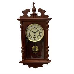 A contemporary 21st century wall clock in a mahogany finished case with a fully glazed door, two-part dial with Roman numerals and steel spade hands, Hermle spring driven eight-day movement with chime/silent feature, visible brass faced pendulum bob.



