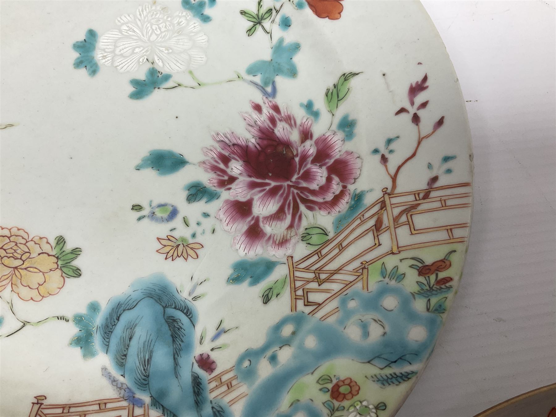 Three 18th century Chinese Famille Rose plates, the first example enamelled with blossoming peonies, rockwork and fence, the other two examples of similar design, decorated with blossoming peonies and sprigs within shaped inner borders, each approximately D23cm
