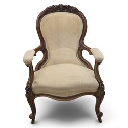 Late Victorian walnut open armchair, the carved shaped cresting rail centred by scrolls and foliage above a padded serpentine back and overstuffed seat upholstered in cream striped fabric, with padded scroll arms on open carved supports, raised on cabriole supports with carved knees and ceramic castors