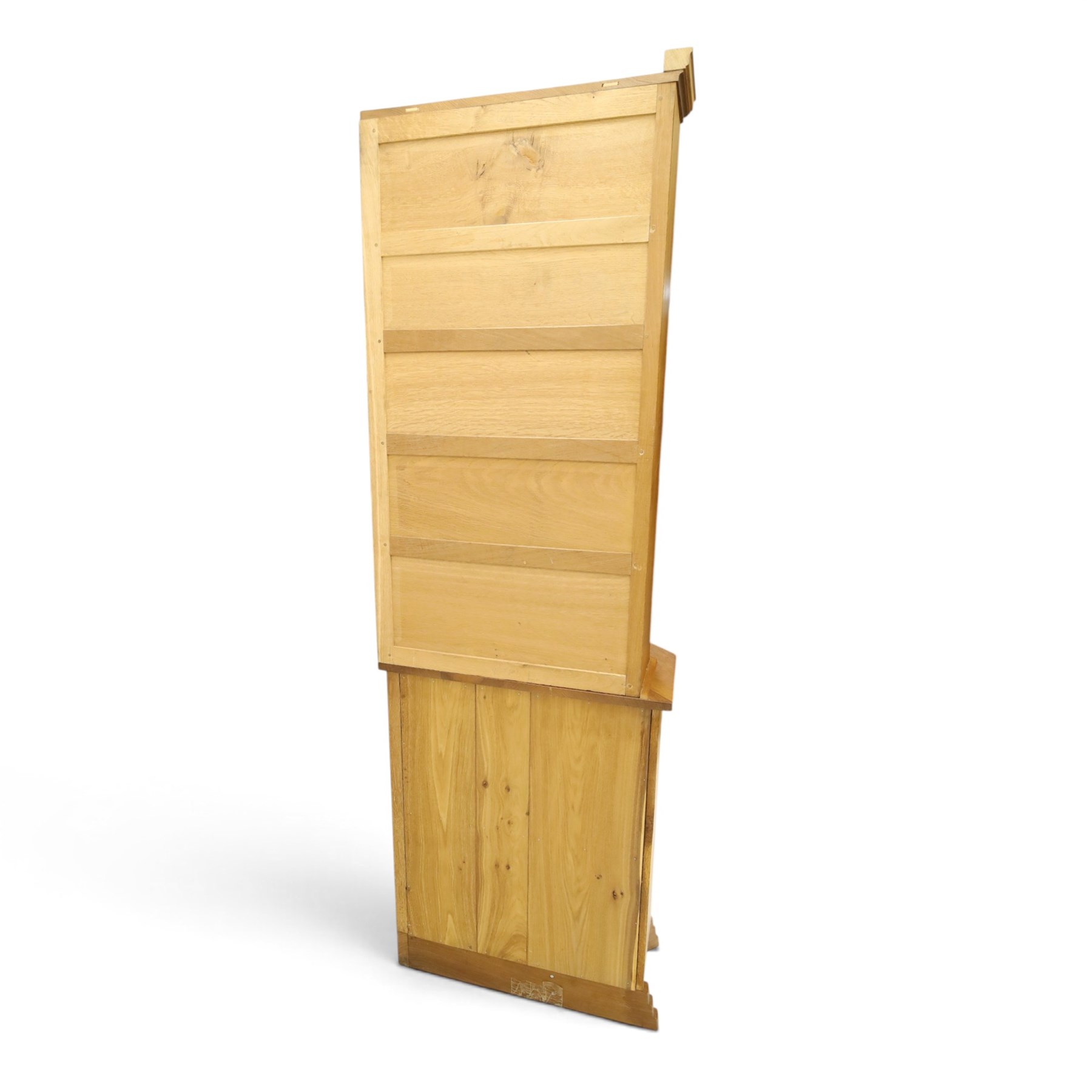 Acorn Industries - oak floor-standing corner cabinet, the top fitted with astragal glazed door enclosing four shaped shelves, the base with single panelled cupboard over two drawers, raised on four stepped feet, carved with acorn signature to top and base, by Alan Grainger, Brandsby