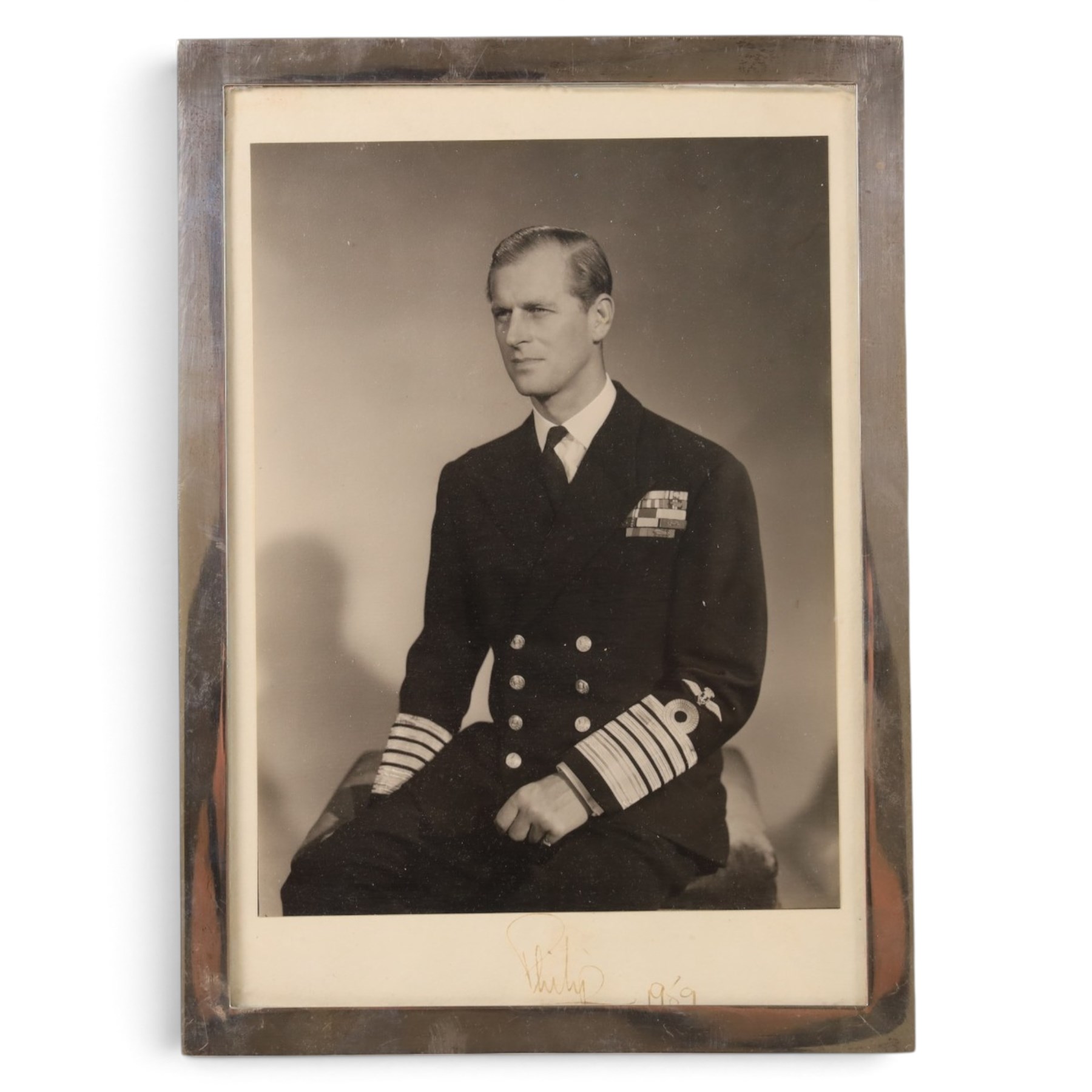 HRH The Duke of Edinburgh signed black and white presentation portrait photograph of Prince Philip wearing Naval uniform, signed in ink on mount ‘Philip 1959’, 20cm x 15cm, contained within a rectangular silver frame, together with a framed photograph of the Prince in India 1959 greeting guests at a formal event and a further black and white photograph