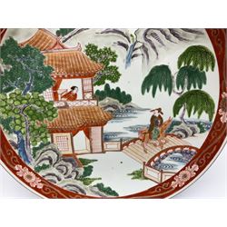 Large 20th century Chinese plate, decorated in polychrome enamels with a figure on horseback traversing a bridge, and figure at the window of a pagoda, within a mountainous landscape, the whole contained within a red border decorated with scrolling foliate motifs, D37cm