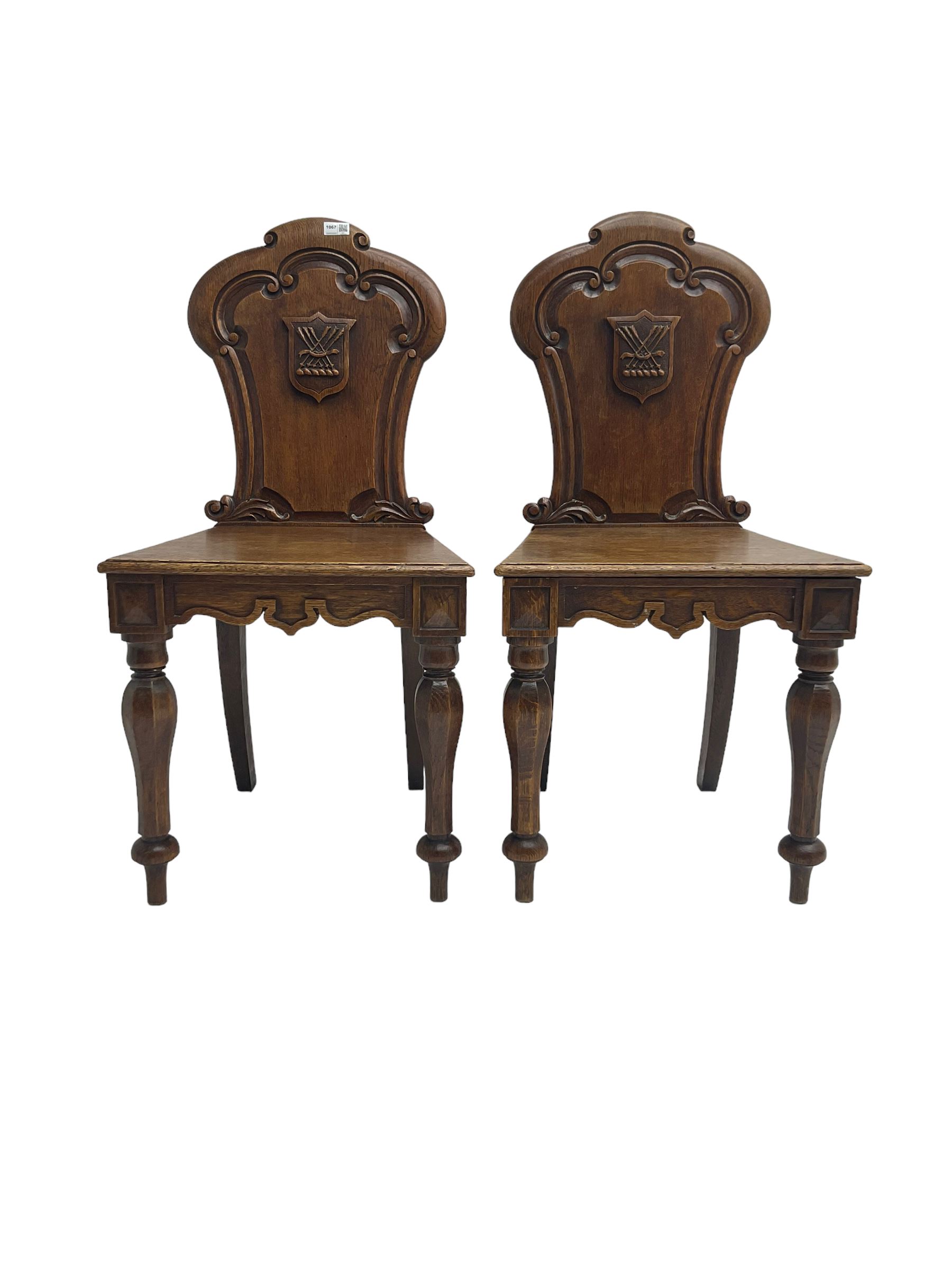 Pair Victorian oak hall chairs, scallop shaped back with carved scrolls and central shield moulding, panel seat over shaped frieze rail, raised on turned supports