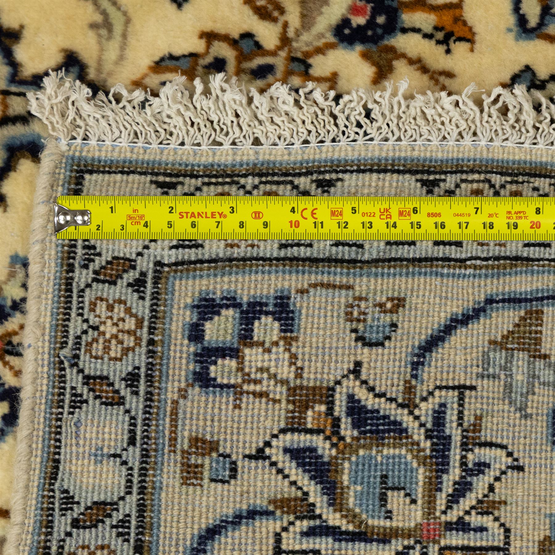 Central Persian Kashan hand-knotted rug, ivory ground, with a small central floral medallion and pendants, the field decorated with fine blue, ochre and beige scrolling vines, flowerheads and palmettes, within an ivory border of repeating floral sprays and meandering vines, flanked by narrow guard stripes, with cotton fringes