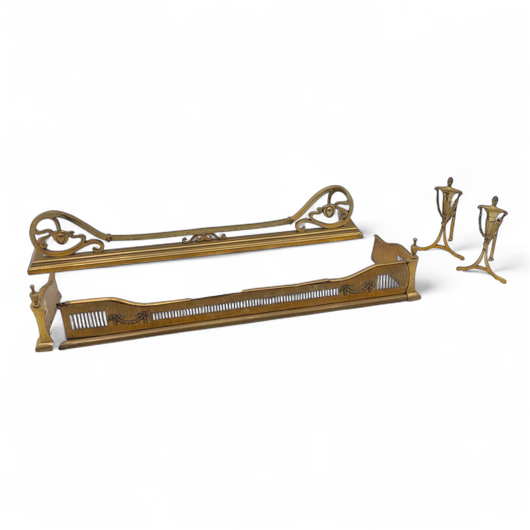20th century fire side items, two brass fire fenders, one of pierced gallery design with urn finials and turned supports, the other with scroll pierced ends and plain moulded rail (H 26cm, W 128cm, D 32cm) (H 23cm, W 134cm, D 21cm) and two brass fire dogs (H 34cm, W 20cm, D 17cm)