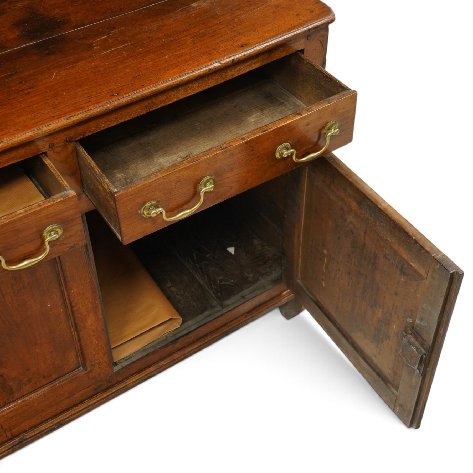 18th century oak dresser with rack, the three-tier plate rack with dentil-carved cornice, the plate shelves with moulded edge and wrought metal hooks, the base fitted with three drawers with brass swan-neck handles over three panelled cupboards, lower moulded edge on stile supports
