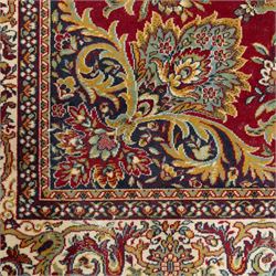 Kashan design carpet, crimson field with central medallion and scrolling floral sprays, cream and polychrome palmette and scrolling vine borders  