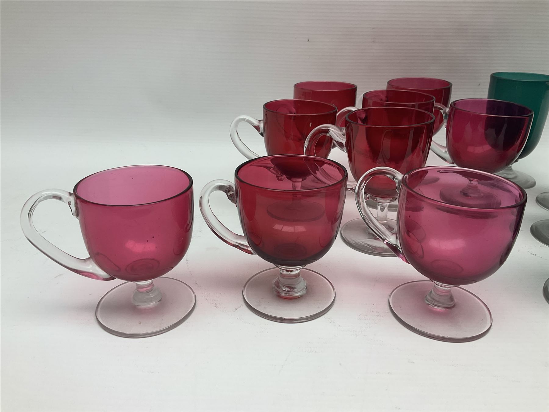 Collection of 19th century coloured glasses, to include nine cranberry glass punch cups, each with clear glass handle and foot and a set of six green glasses, with short clear stems, tallest H10cm