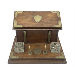 Edwardian oak and brass mounted desk stand, the brass pen rest over vacant brass cartouche, flanked two glass inkwells (lacking covers), before a stationary box, the hinged sloped lid with conforming vacant cartouche opening to reveal a fitted interior, H21.5cm L31.5cm D24cm