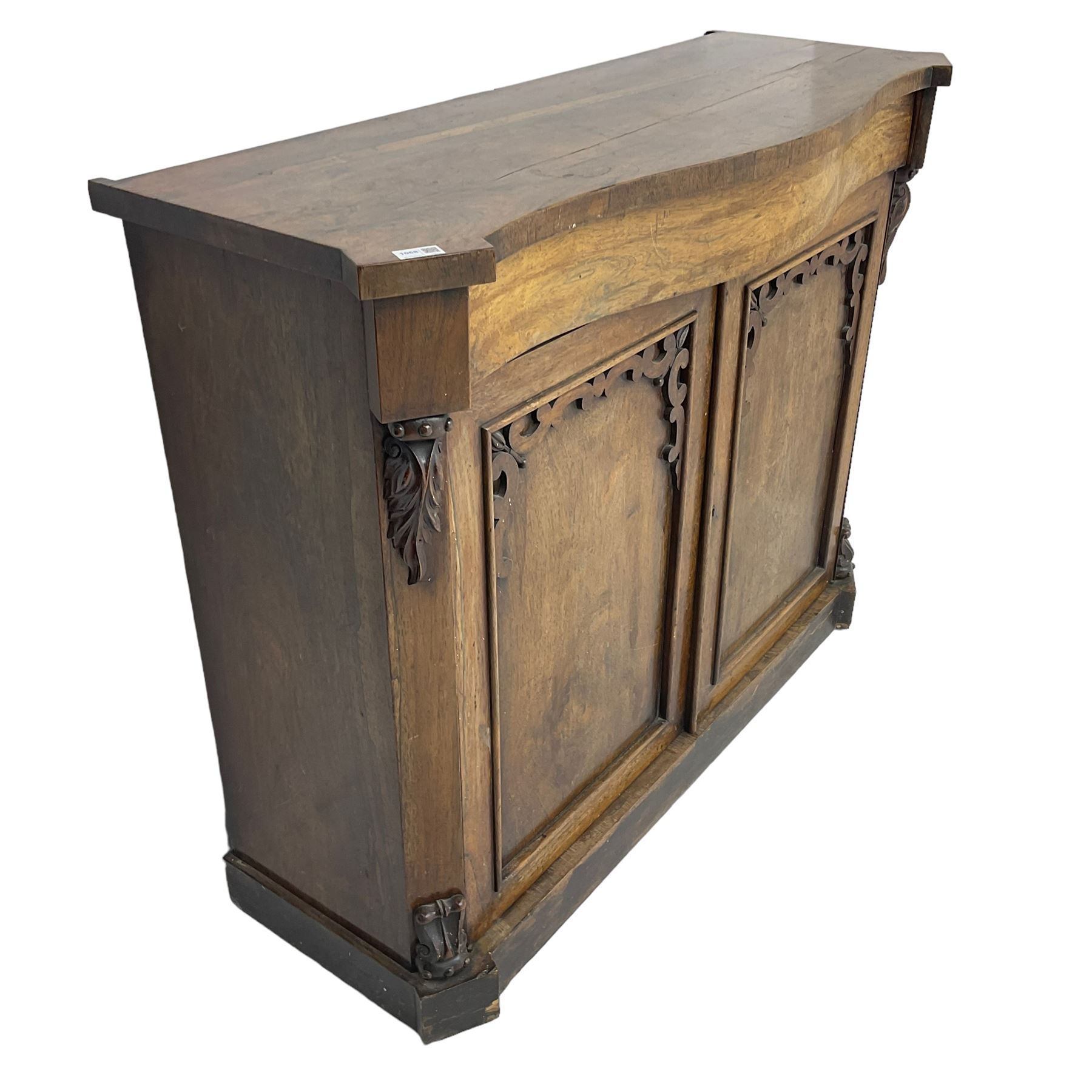William IV rosewood serpentine chiffonier, fitted with frieze drawer over two panelled cupboard doors with applied C-scroll decoration, flanked by canted uprights with moulded foliate corbels