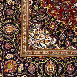 Central Persian Kashan hand-knotted carpet, crimson ground, with a central ivory shaped floral medallion with pendants, surrounded by dense scrolling foliate and floral motifs incorporating rosettes, palmettes and delicate vine work, enclosed by ivory spandrels and a dark navy border with repeating palmettes and meandering vines, flanked by floral guard stripes, with cotton fringes