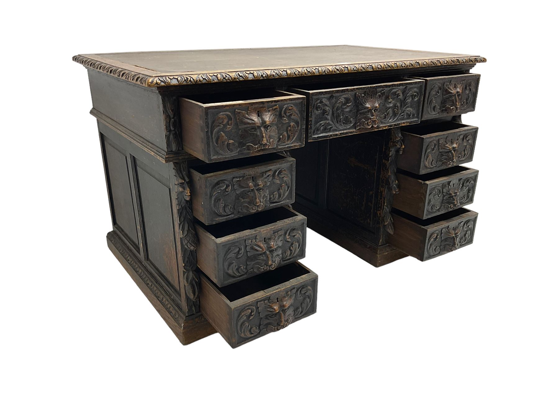 Late 19th century Gothic revival carved oak twin pedestal desk, rectangular top with inset writing surface and carved edges, central frieze drawer flanked by eight drawers, all with green man carved handles and extending trailing foliage, carvings of pineapple and lion mask corbels, the pedestals with panelled sides and back, on plinth bases