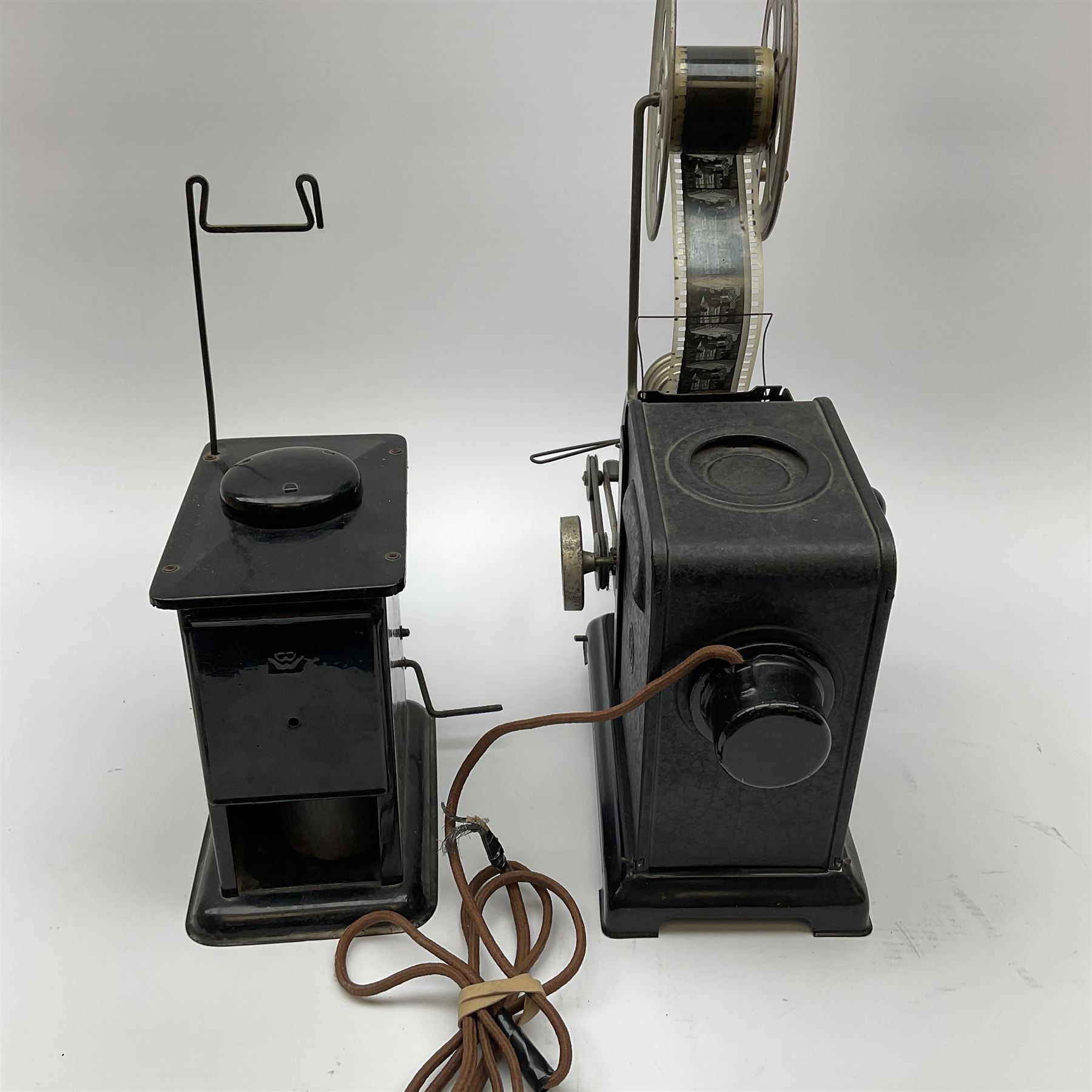 Early 20th century tinplate combined magic lantern and 35mm cinematograph projector, hand-cranked, with electric bayonet lamp, fitted with film reels, L35cm overall, and a similar projector by Gebruder Bing Nuremberg with spirit lamp (glass chimney a/f) L22cm, with two reels of film 