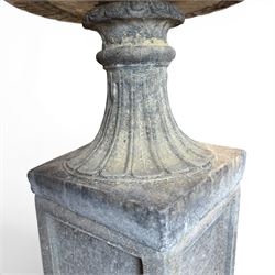 Pair of cast stone garden urns of kylix form on pedestals, the broad egg-and-dart moulded rim over a shallow gadrooned underbelly, with waisted tapering base, raised on matching plinth bases with faux panelled facia