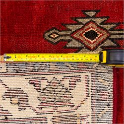 West Persian Mazlaghan hand-knotted rug, madder red field with central stepped lozenge medallion with pendant motifs flanked by angular serrated spandrels filled with small geometric devices, enclosed within multiple borders featuring stylized floral and geometric motifs, with cotton fringe ends 