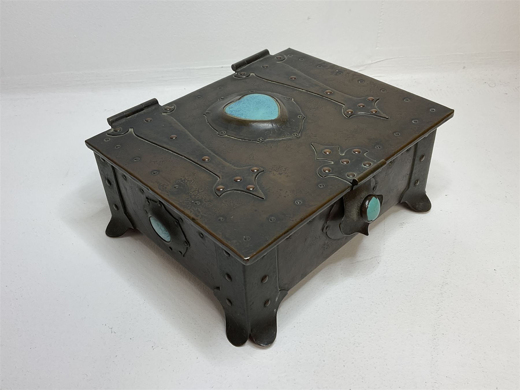 Arts and Crafts copper box, the lid decorated with stylised riveted hinges and inset with Ruskin type ceramic turquoise heart-shaped cabochon, the mount etched M.B 1913, and further cabochon roundel to each side panel, including one inset to the clasp acting as the knob to the locking mechanism, marked RS Douglas 1913 beneath, W16.5cm H7cm D15cm