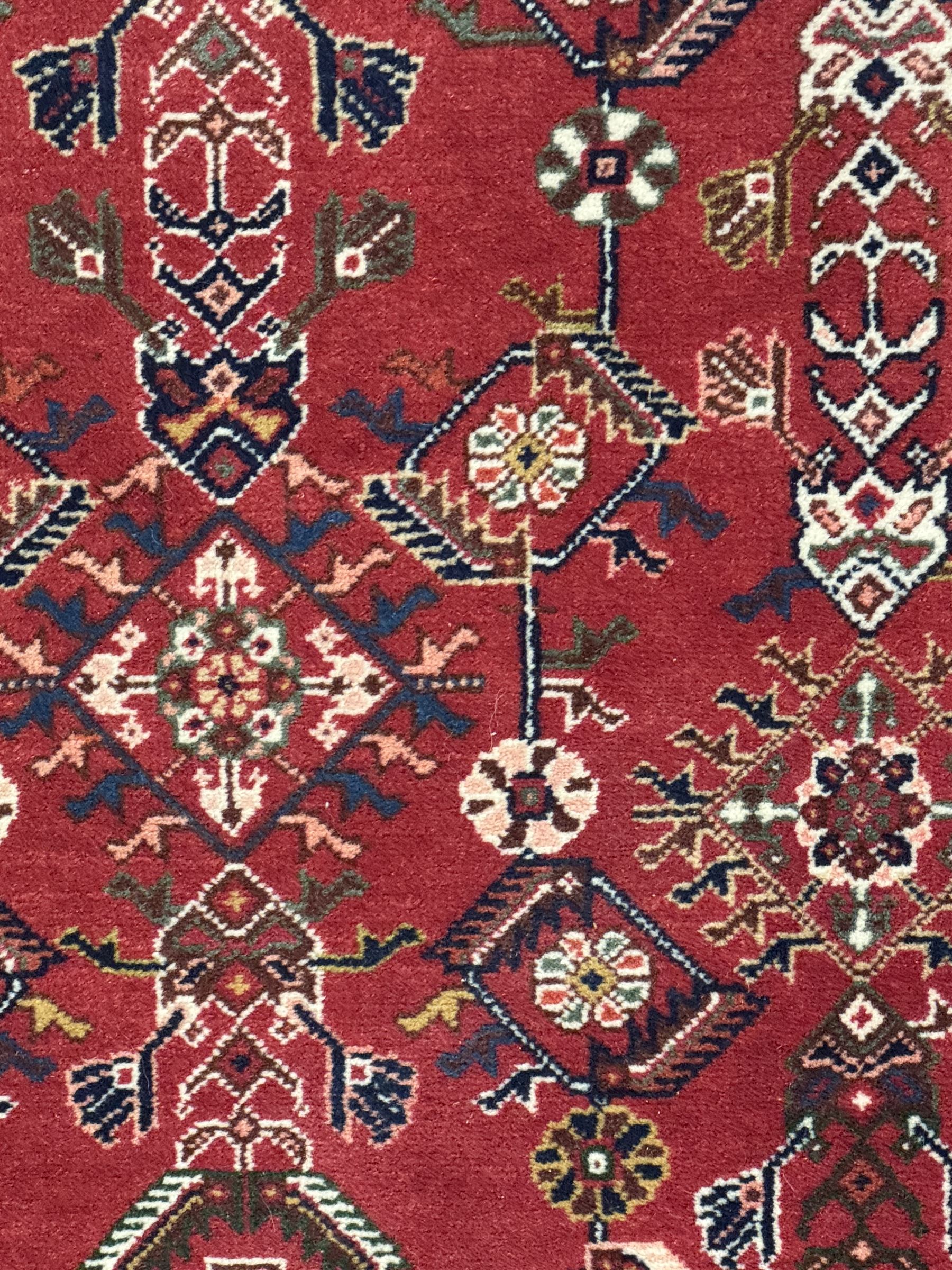 Persian Qashqai crimson ground runner, the central field decorated with three large geometric medallions with intricate angular and floral motifs, the indigo spandrels with complementary geometric designs, bordered by an ivory band with repeating floral patterns and angular vines