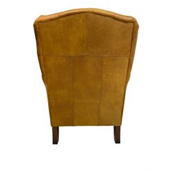 Georgian design armchair, upholstered in buttoned tan leather with over-stuffed seat and scrolled arms, raised on turned tapering front feet