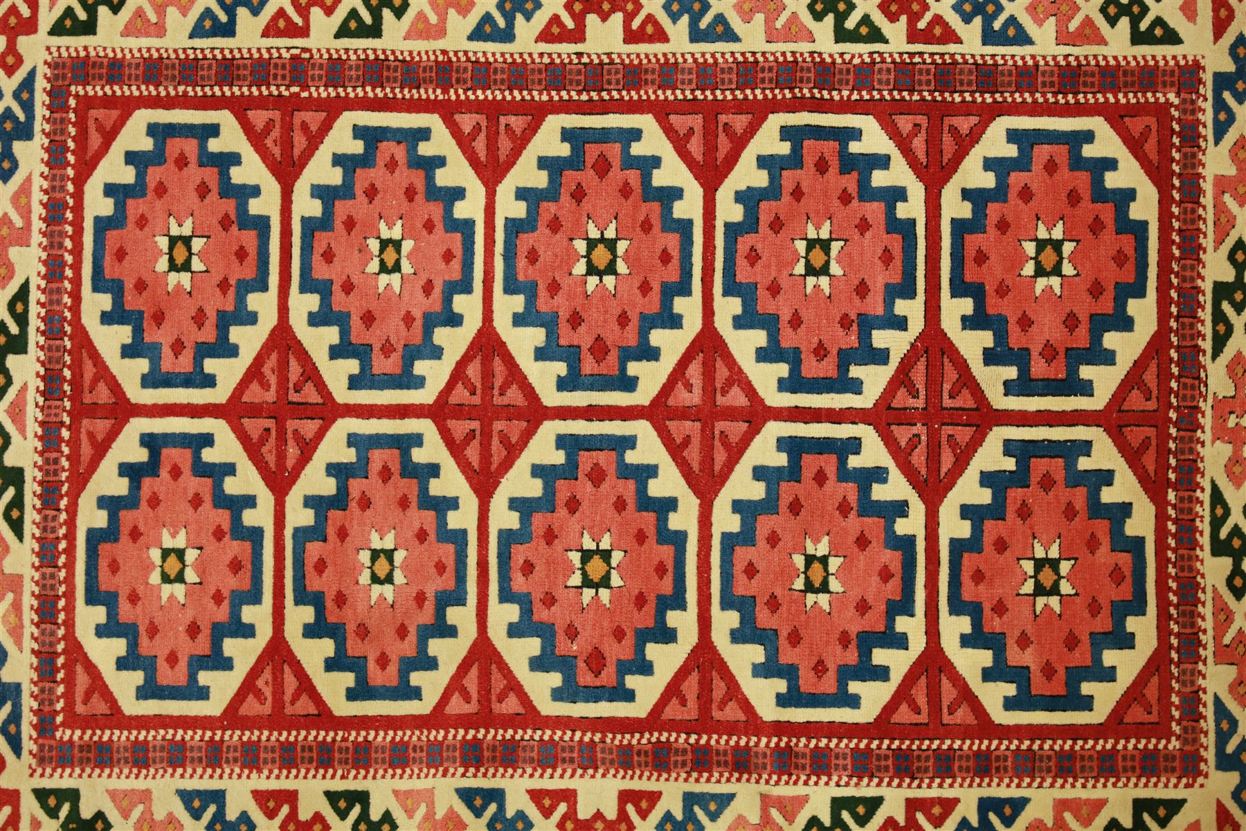 Anatolian Soumak rug, ivory ground decorated with a grid of eight octagonal medallions in terracotta red outlined in blue, centered with a star motif in vertical rows, framed by a series of geometric borders in ivory, green, and blue, incorporating hooked devices and stylized lozenges and stripped end panels, with signature at either end 